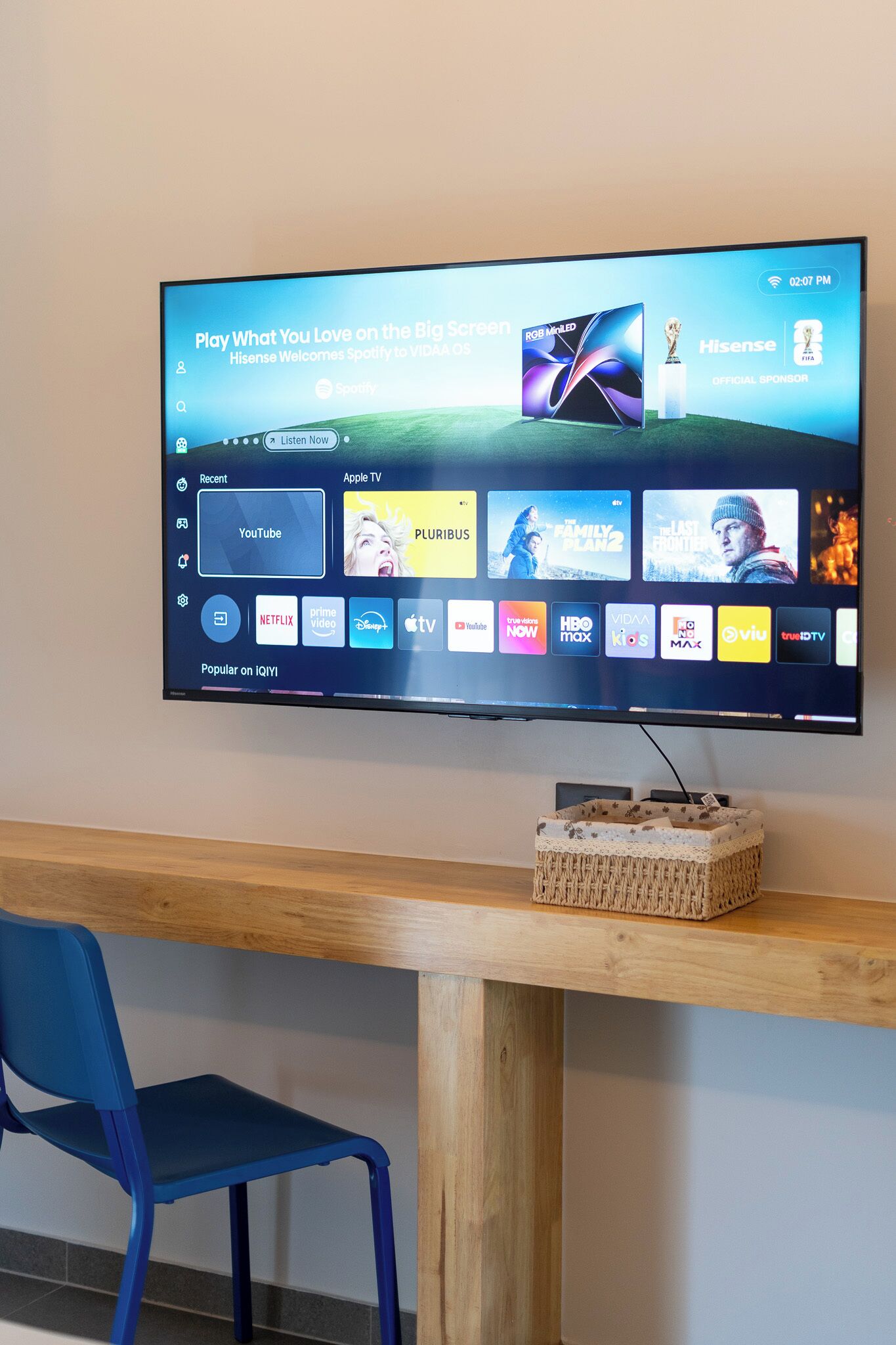 A flat-screen TV mounted on a wall displaying a streaming service interface with various content options.