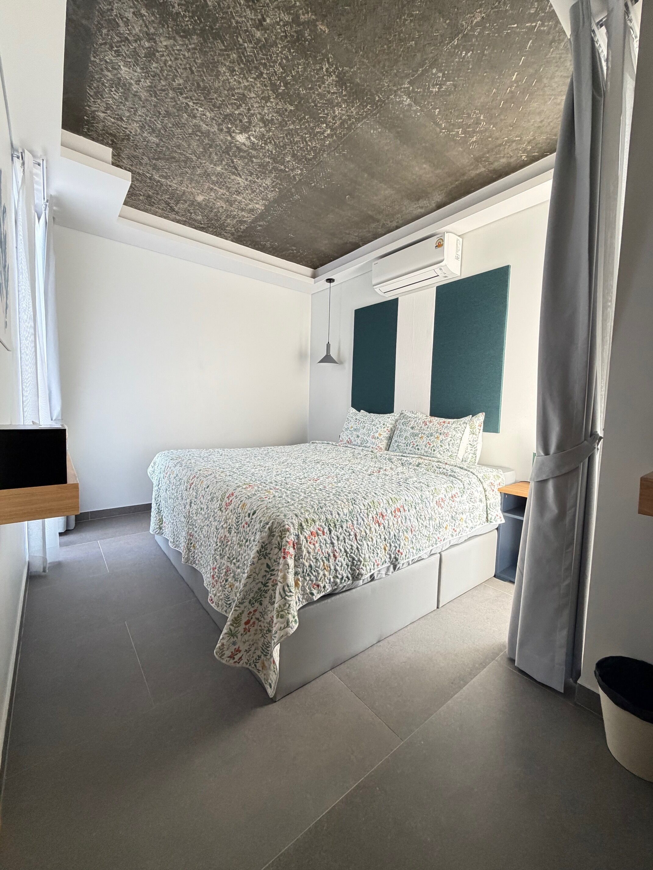 Una camera da letto con un letto, un comodino, un cestino e una finestra con tende.