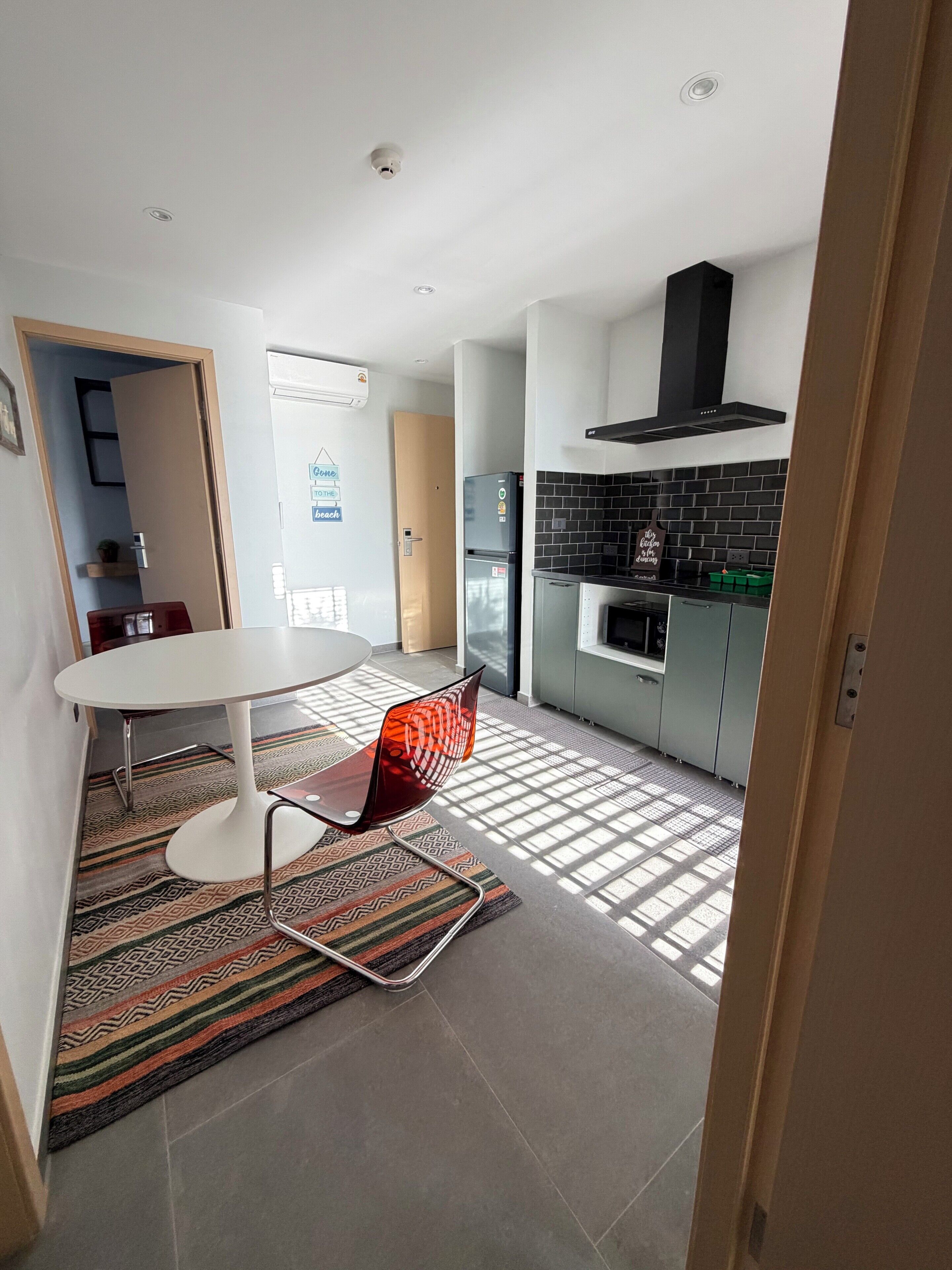 A modern kitchen with a black range hood, a dining area with a white table and a red chair, and a patterned rug on the floor.