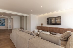 Ein modernes Wohnzimmer mit einem Ecksofa, einem flachbildfernseher an der Wand und einer Holzkassette.