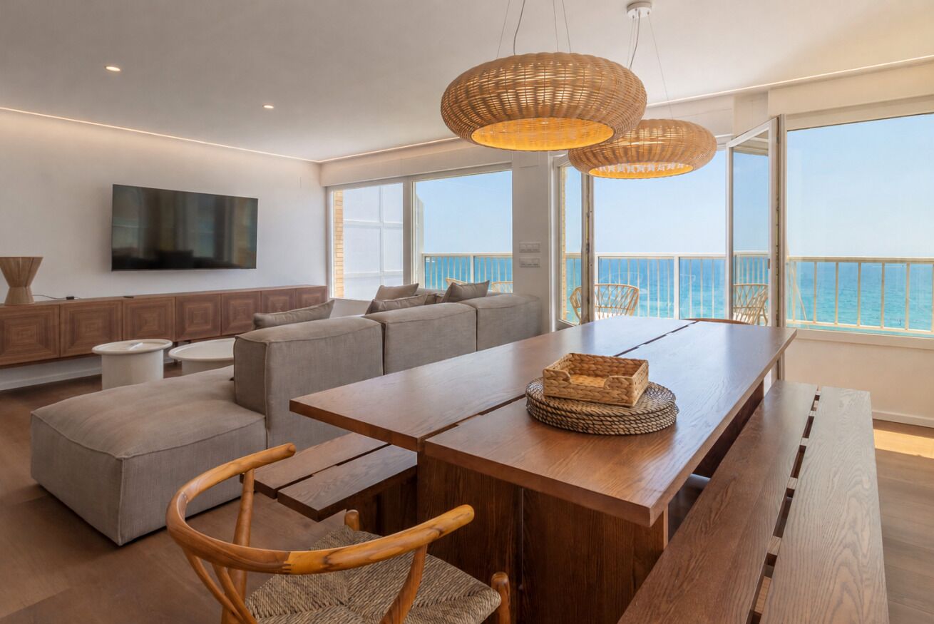 A modern living room with a wooden dining table, grey sofas, and wicker pendant lights.