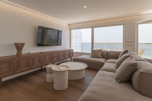 A modern living room with a sectional sofa, a wooden cabinet, and a flat-screen TV. - Your beachfront home in Calpe: the perfect retreat for every season.Imagine waking up every morning to the golden Mediterranean light flooding your home, gazing at the breathtaking silhouette of the Peñón de Ifach while enjoying a peaceful coffee on yo (Calp)