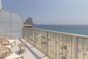 Ein Balkon mit Korbmöbeln, der Blick auf einen Strand mit Sonnenschirmen und Palmen bietet.