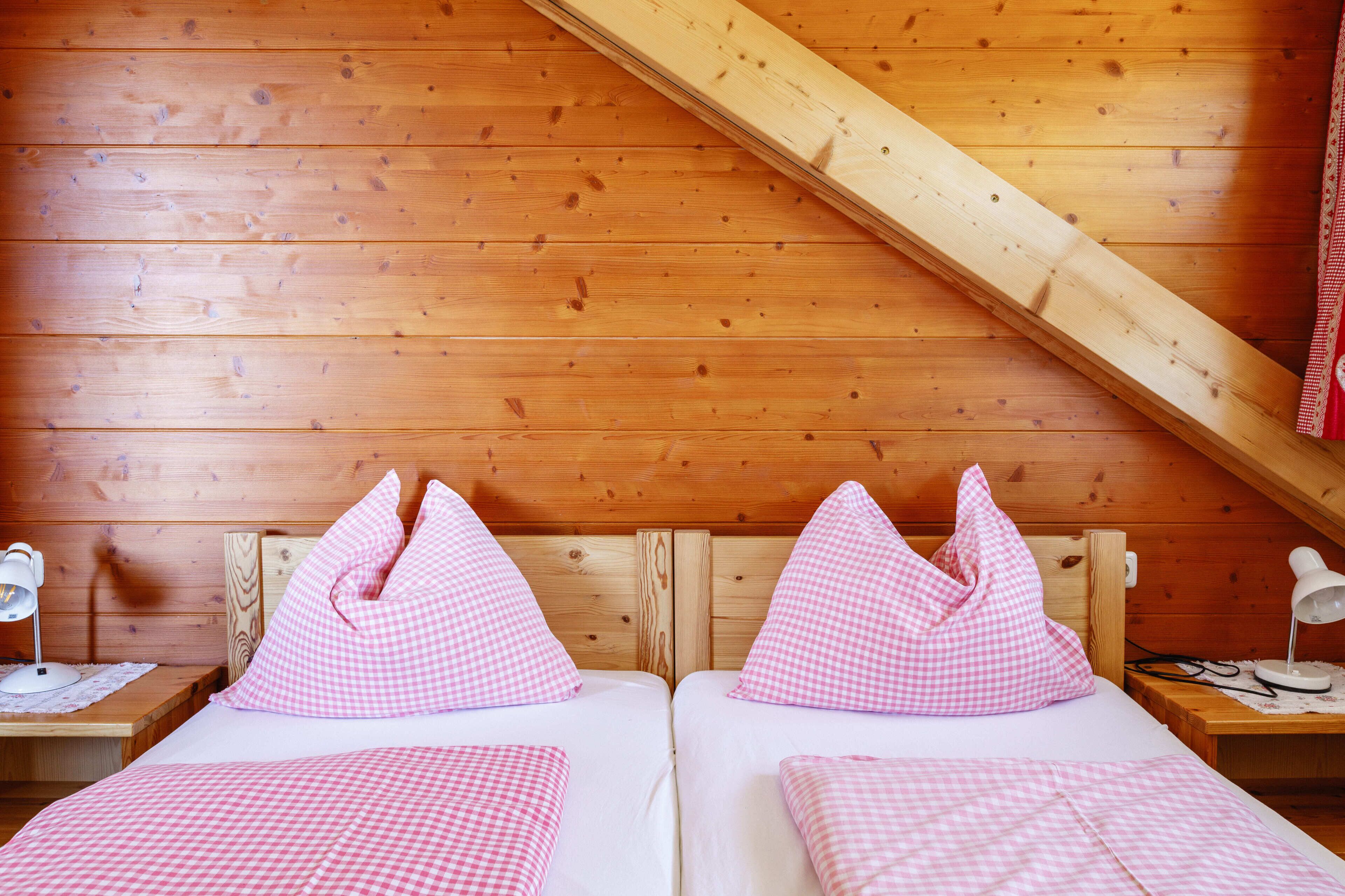 Een kamer met twee bedden, houten wanden, een schuine plafond en een nachtkastje met een lamp.