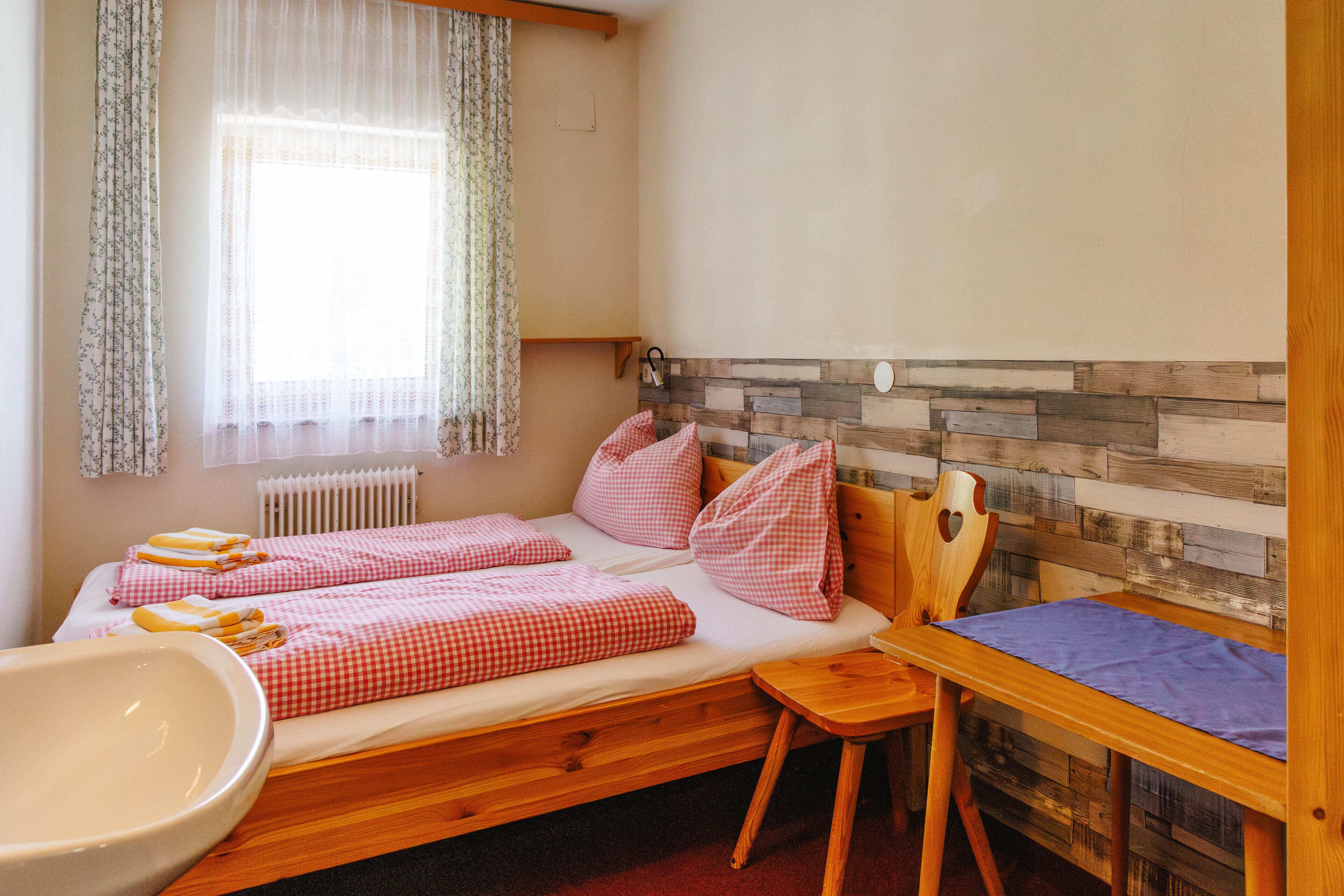 Una cama individual con ropa de cama a cuadros, cabecera de madera, una mesita pequeña y un radiador.