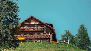 A wooden building with balconies, labeled 'TH.K.HOLLAUS,' and a sign for 'SCHIVERLEIH SCHISERVICE.'