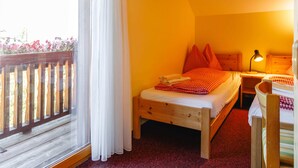 Quarto com cama de madeira, mesa de cabeceira, abajur e vista para flores pela janela.
