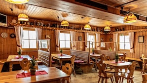 Um interior rústico em madeira, com diversas opções de assento, incluindo mesas e bancos, e vários objetos decorativos nas paredes.