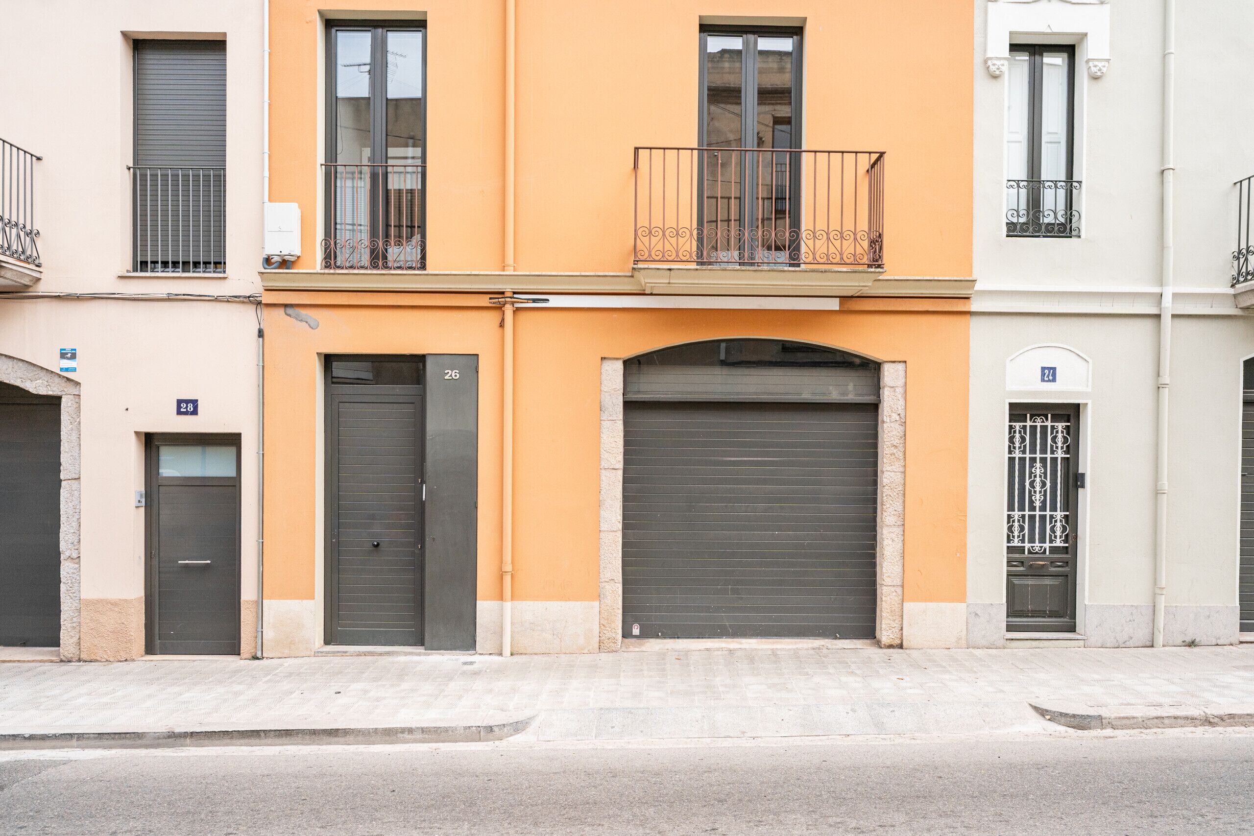 Ein mehrstöckiges Gebäude mit geschlossenen Rollläden, einem Balkon mit schmiedeeisernen Geländern und einer Straße davor.