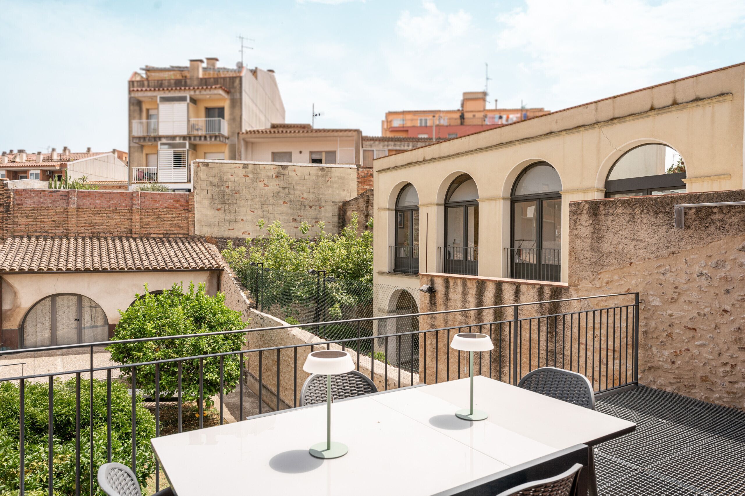 Una terraza en la azotea con mesa y sillas, rodeada por una barandilla metálica y vistas panorámicas de la ciudad.