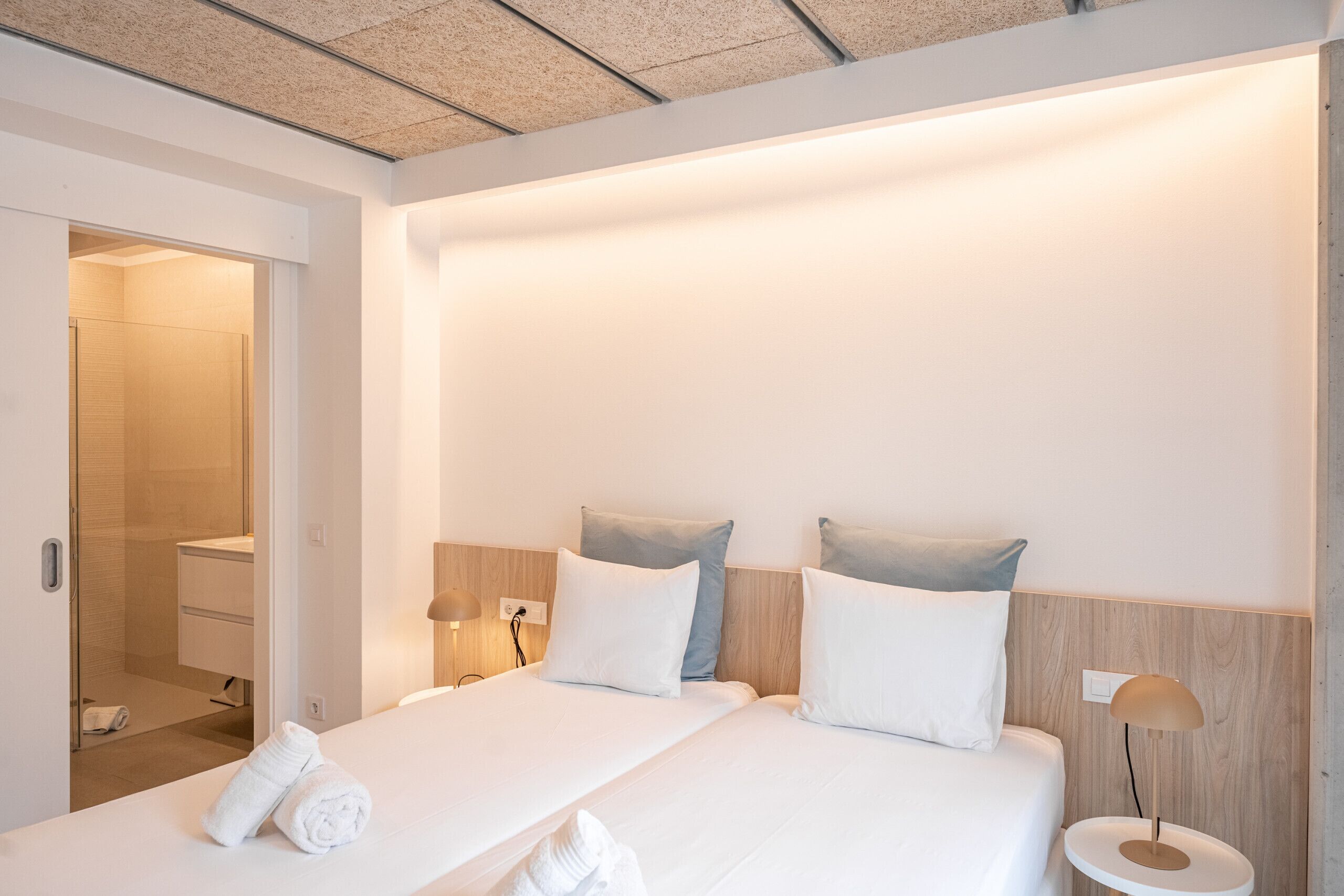Een hotelkamer met een bed, bedlampen, een nachtkastje en een zichtbare badkamer door een open deur.