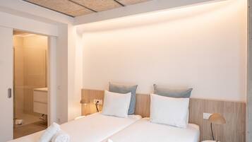 Een hotelkamer met een bed, bedlampen, een nachtkastje en een zichtbare badkamer door een open deur.