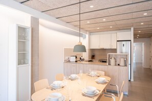 A modern kitchen with a central island, white cabinetry, and a dining area set for six with a table, chairs, and dinnerware.