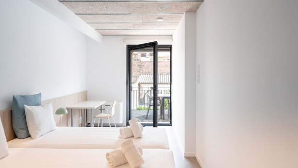 A hotel room with two beds, a small table, and a view of the outside balcony. - Majordoms Llimoner 1 - Figueres (Figueres)