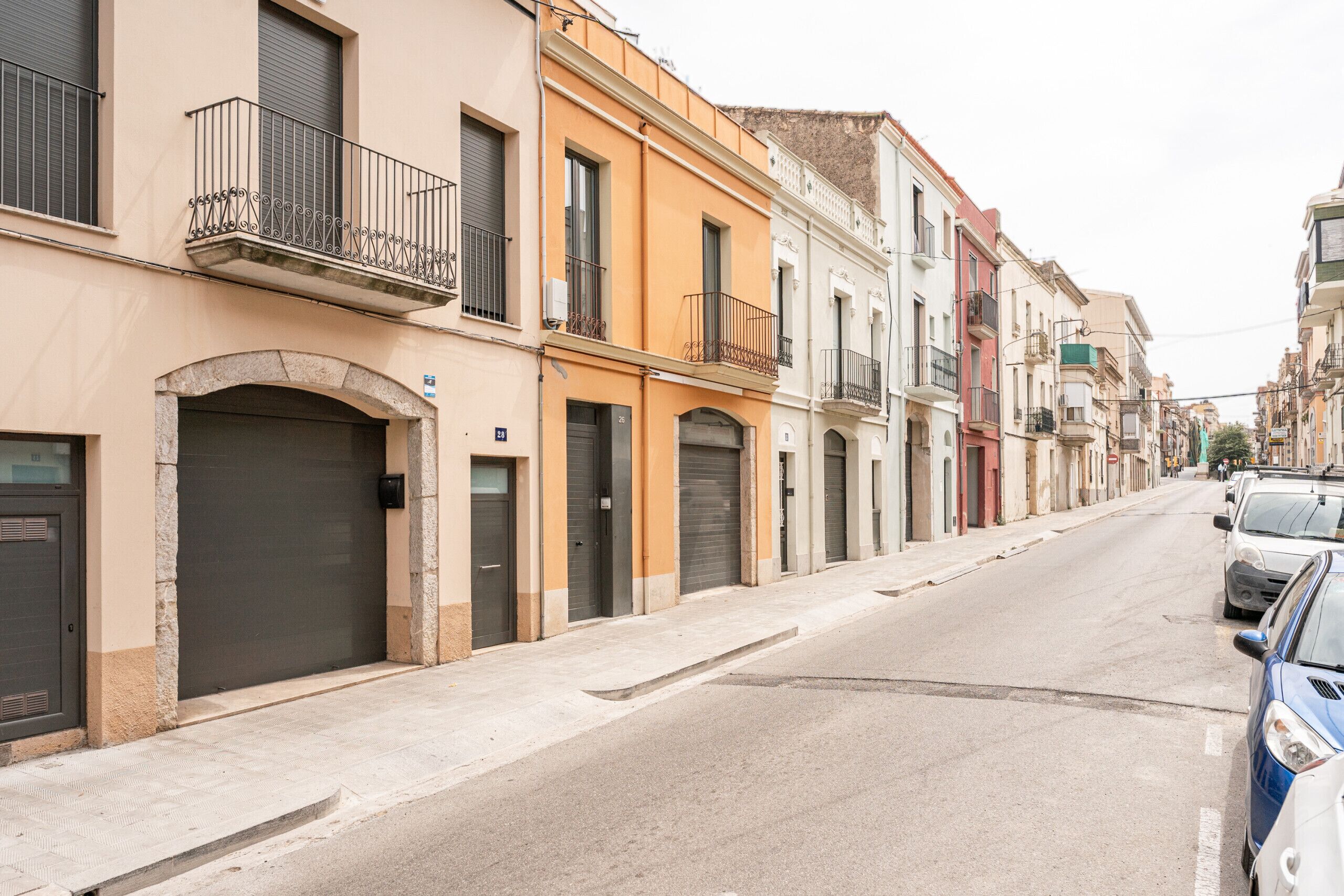 Una calle con edificios, algunos con contraventanas cerradas, y coches estacionados.