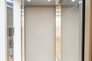 Et moderne elevatormiljø med metalvægge og et kontrolpanel til venstre.