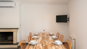Ein Essbereich mit einem langen Holztisch, gedeckt für eine Mahlzeit, umgeben von orangefarbenen Stühlen, einem Kamin und einem an der Wand befestigten Fernseher.
