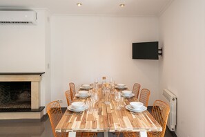 A dining area with a long wooden table set for a meal, surrounded by orange chairs, a fireplace, and a mounted television on the wall. - Majordoms Ponent, Banyoles (Banyoles)