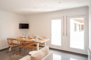 A dining area with a table set for four, orange wireframe chairs, a flat-screen TV mounted on the wall, and a sliding glass door leading to an outdoor area. - Majordoms Ponent, Banyoles (Banyoles)