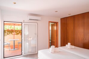 A hotel room with a bed, a wooden wardrobe, a sliding glass door to a balcony with a table and chairs, and an air conditioning unit. - Majordoms Ponent, Banyoles (Banyoles)