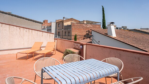Eine Dachterrasse mit Tisch und Stühlen, Blick auf die Stadtlandschaft und einem wolkenlosen Himmel.
