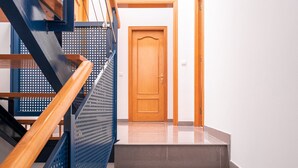 Eine Treppe mit einem hölzernen Geländer und einem blauen Metallschutzgeländer, die zu einer Holztür führt.