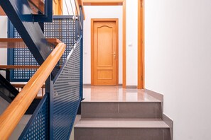 A staircase with a wooden handrail and a blue metal guardrail, leading to a wooden door. - Majordoms Ponent, Banyoles (Banyoles)