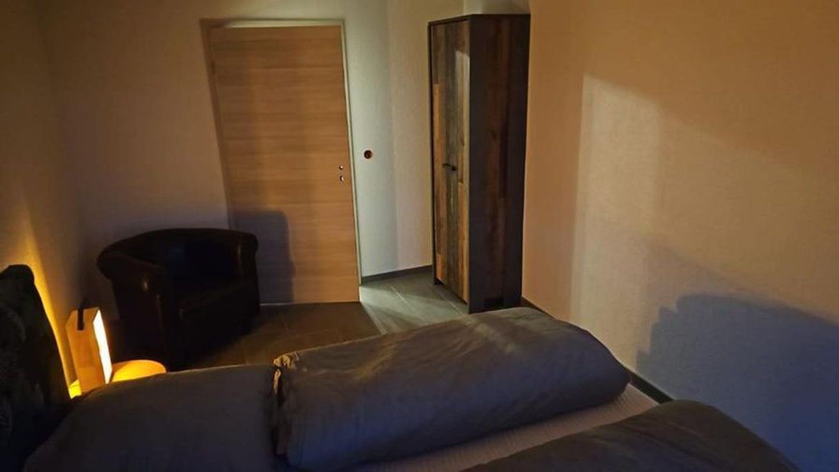 Ein Zimmer mit einem Bett, einem Schrank und einem Schreibtisch mit einer Lampe.