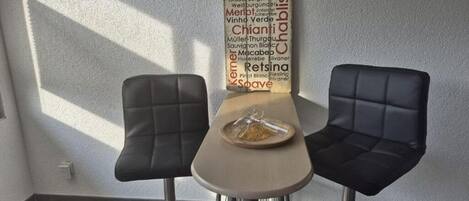 Un comedor con dos sillas negras y una mesa, una carta de vinos colgada en la pared, y un plato con comida sobre la mesa.