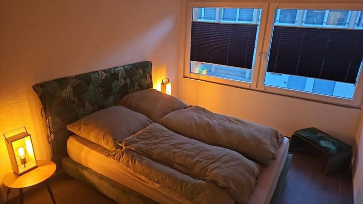 A bed with a headboard, two bedside lamps, and a window with blinds.