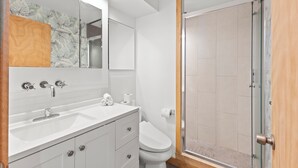 A modern bathroom with a white sink, mirror, and toilet, and a glass shower enclosure. - Ilikai Marina - Modern Designer Studio (Honolulu)