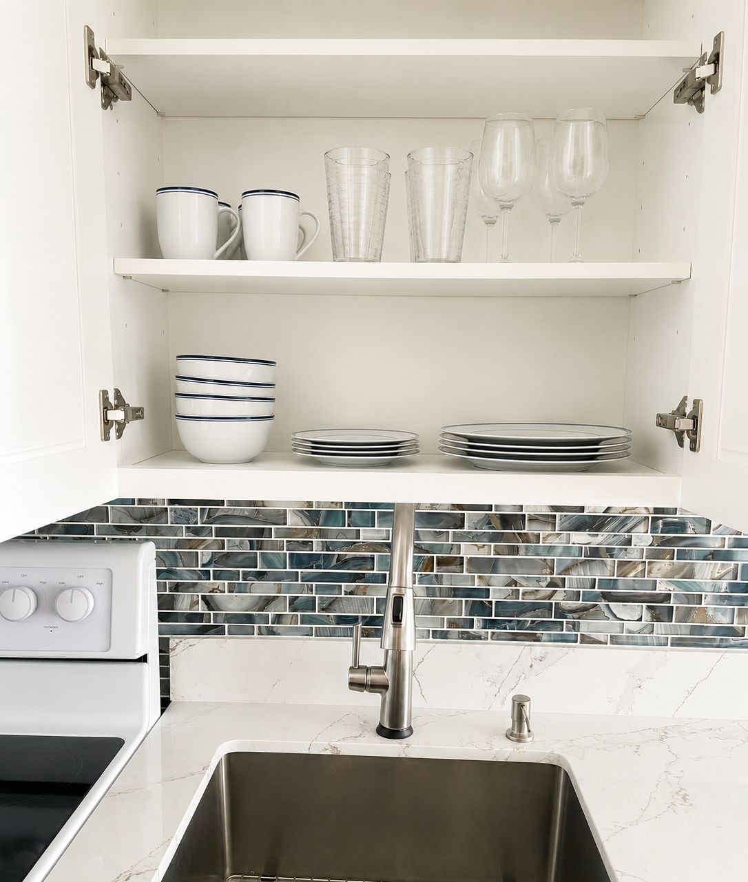 Una cocina con estufa integrada, un lavamanos y salpicadero con azulejos azules y blancos.