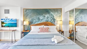 A hotel room with a large bed, two bedside tables with lamps, a view of the ocean, a painting on the wall, and a mirror on the opposite wall. - Ilikai Marina - Modern Designer Studio (Honolulu)
