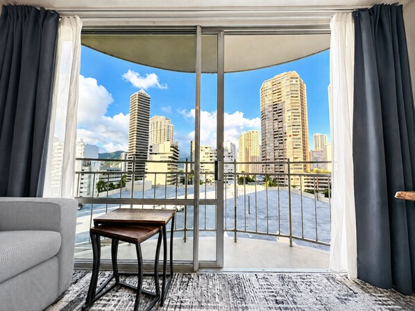 Una sala de estar moderna con un gran ventanal corredizo que da a un balcón y vistas a la ciudad.