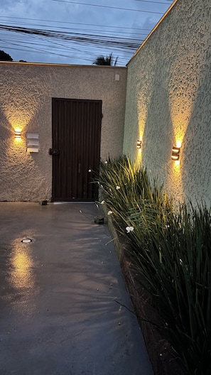 Entrada de edifício com parede texturizada, porta escura e duas luminárias fixadas na parede.