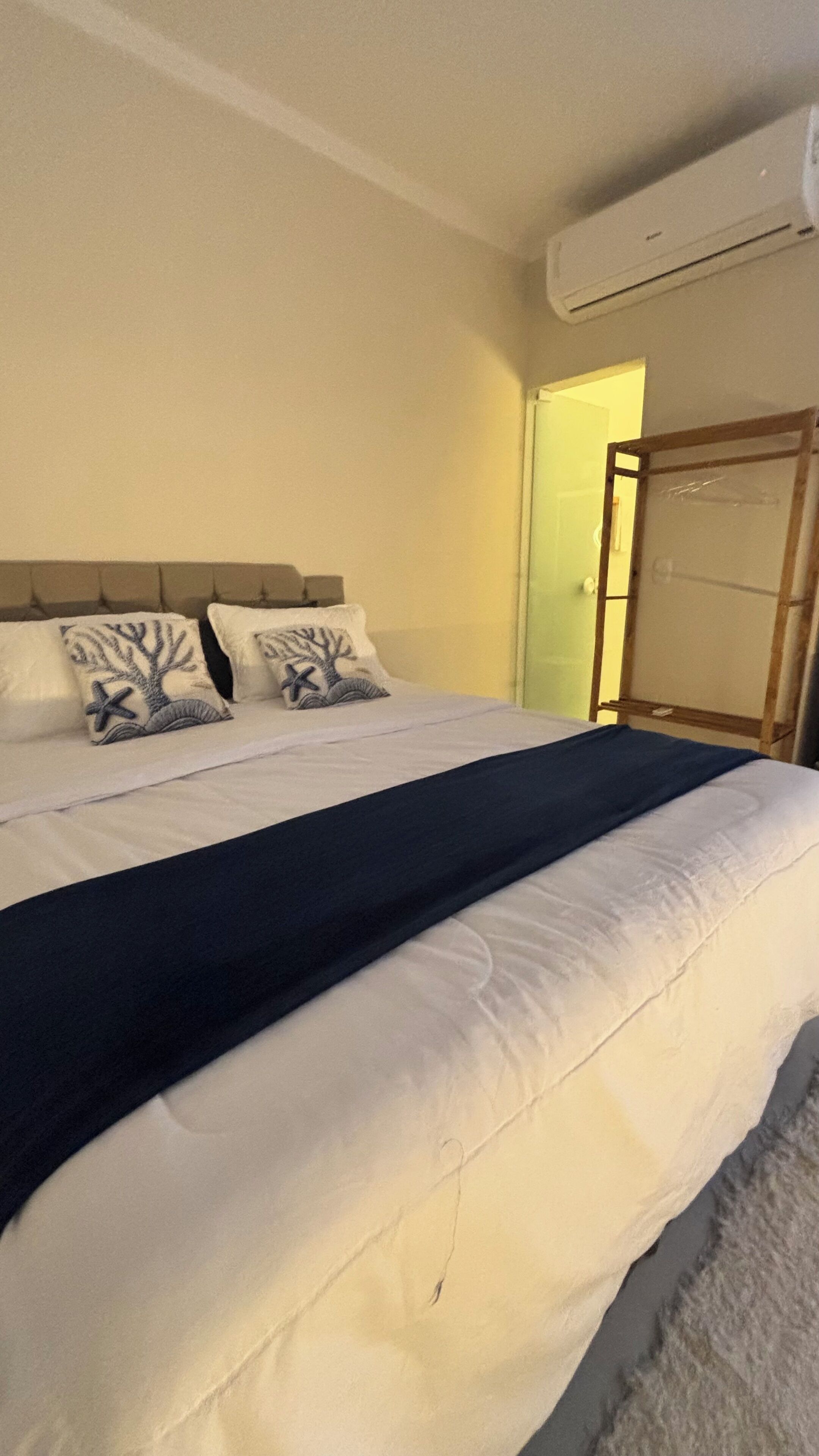 A bed with a headboard, two pillows with a tree and starfish design, a dark blue blanket, and an air conditioning unit on the wall.