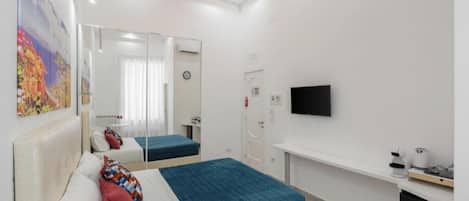 A modern hotel room with a bed, a TV, a desk, and a mirror.