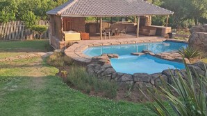 Un patio trasero con piscina, un porche cubierto y un muro de piedra.