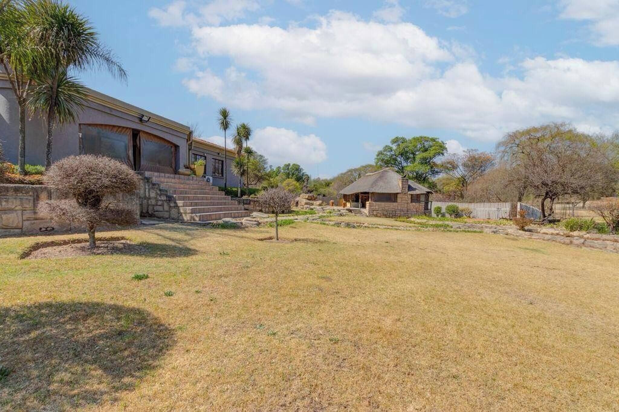 A house with a stone staircase, a thatched-roof structure, and a well-maintained lawn.