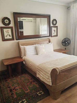 A bedroom with a wooden bed, a large mirror, two bedside tables, a floor fan, and a patterned rug. - Aaybee Recreational Place (Johannesburg)