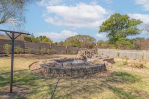 A fenced outdoor area with a stone structure, a wooden swing set, and a metal pergola. - Aaybee Recreational Place (Johannesburg)