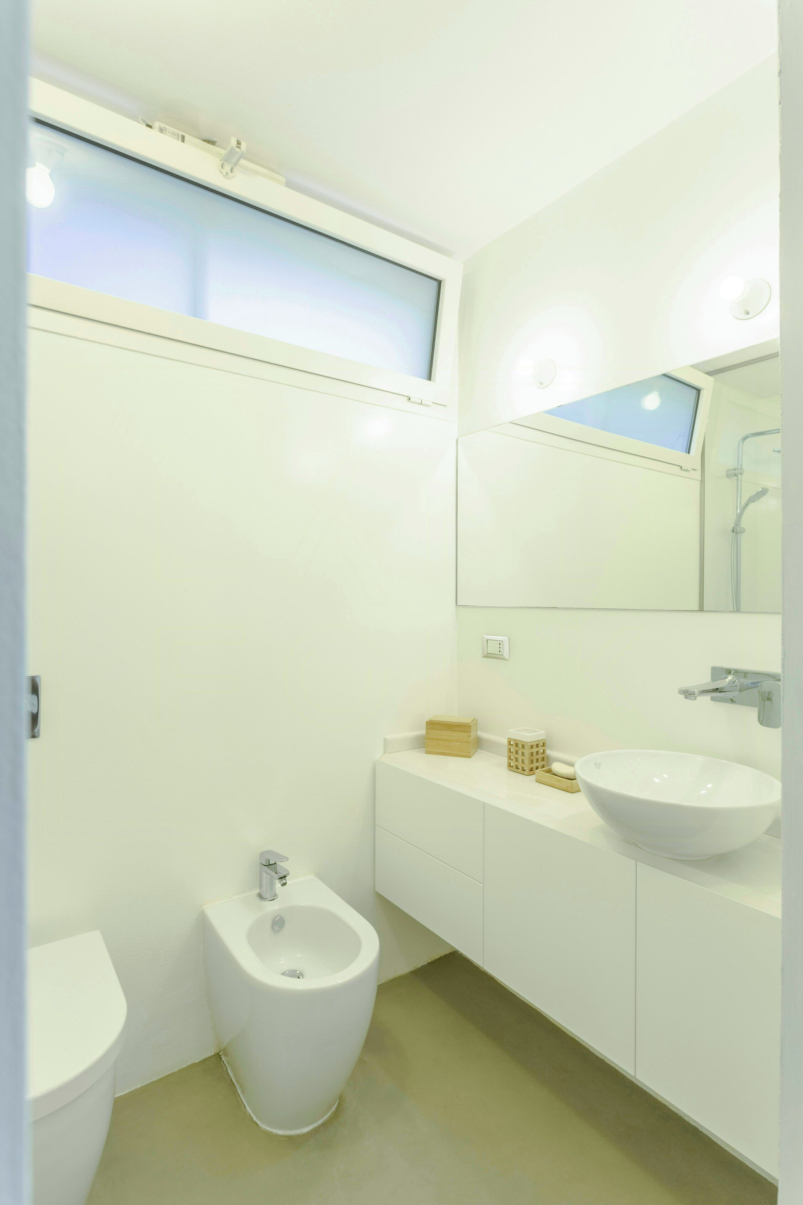 A modern bathroom with a bidet, a sink, a mirror, and a window.