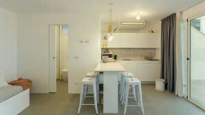 Cozinha moderna com armários brancos, uma ilha central com banquetas e vista para o exterior.