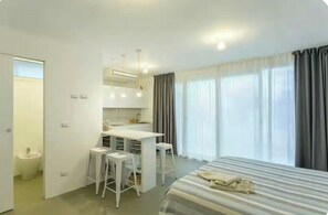 A hotel room with a bed, a desk with a chair, a small stool, a mirror, and a window with curtains. - Studio between Cefalù and the Madonie (Cefalù)