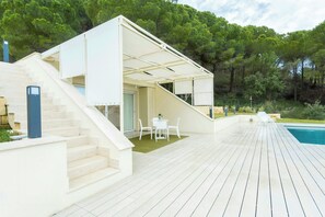 Una casa moderna con una terraza de madera, una piscina y una escalera que lleva a un espacio exterior cubierto.