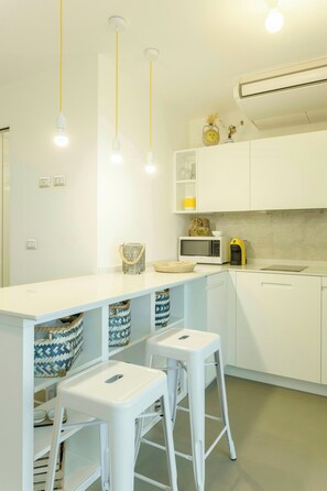 A modern kitchen with white cabinetry, a central island with stools, overhead pendant lighting, and a microwave on the countertop. - Studio between Cefalù and the Madonie (Cefalù)