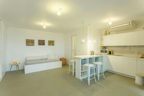 Una cocina moderna con armarios blancos, un comedor con taburetes y un sofá con cojines.