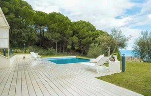 A wooden deck with a swimming pool, lounge chairs, and a view of a forested area. - Studio between Cefalù and the Madonie (Cefalù)
