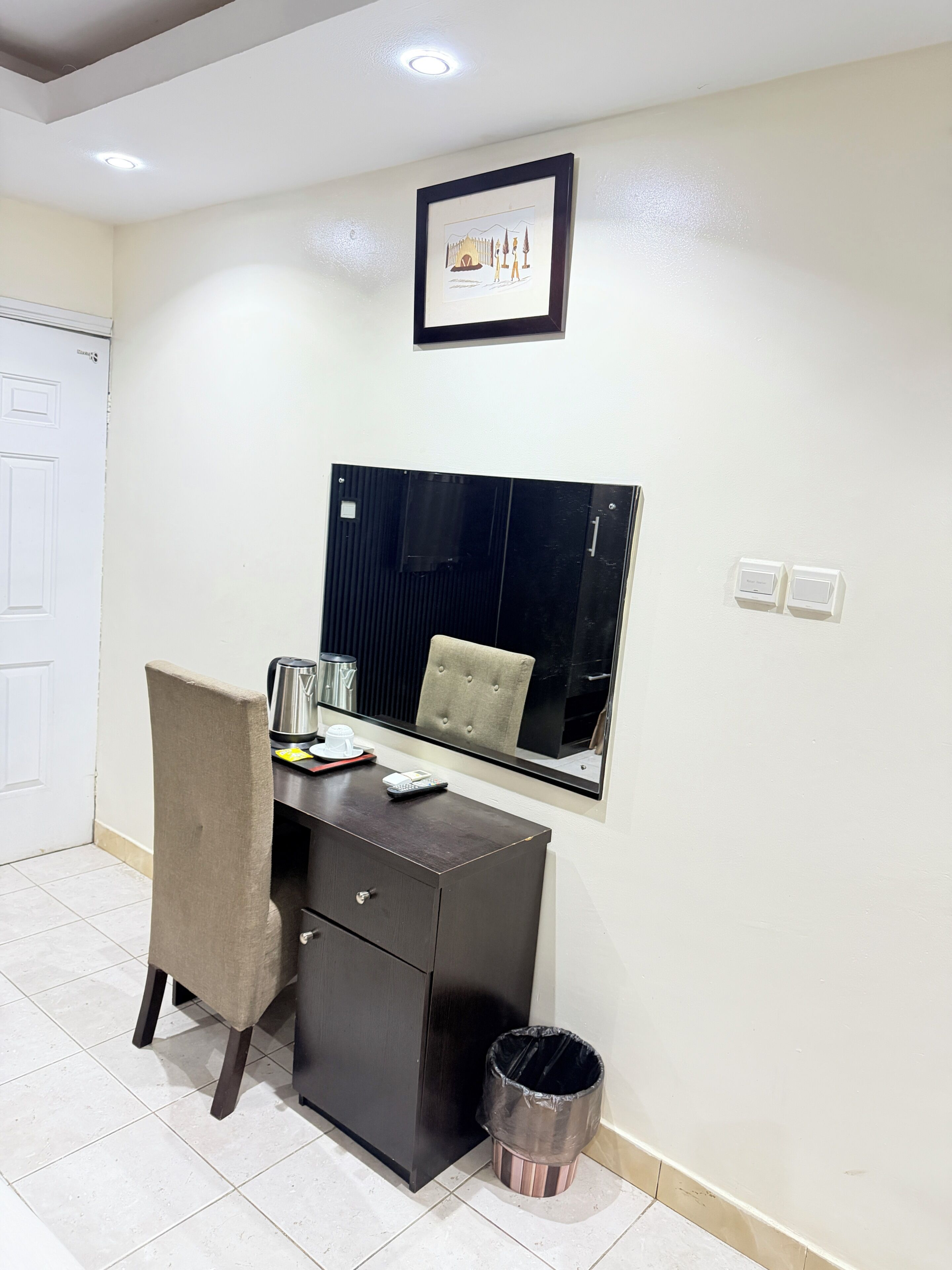 A room with a desk, chair, and a trash bin.