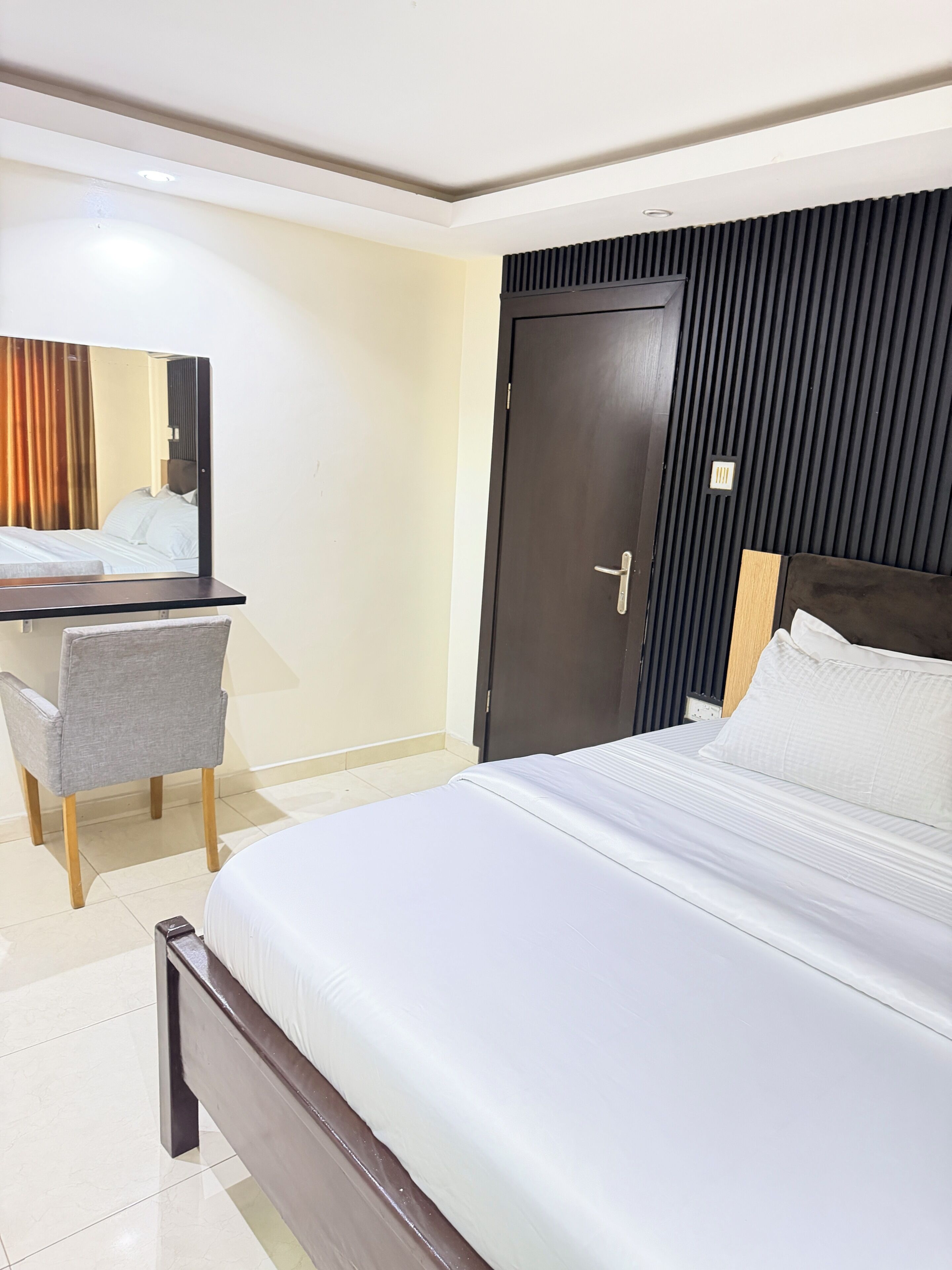 Una habitación de hotel con cama, escritorio, silla, armario y espejo.